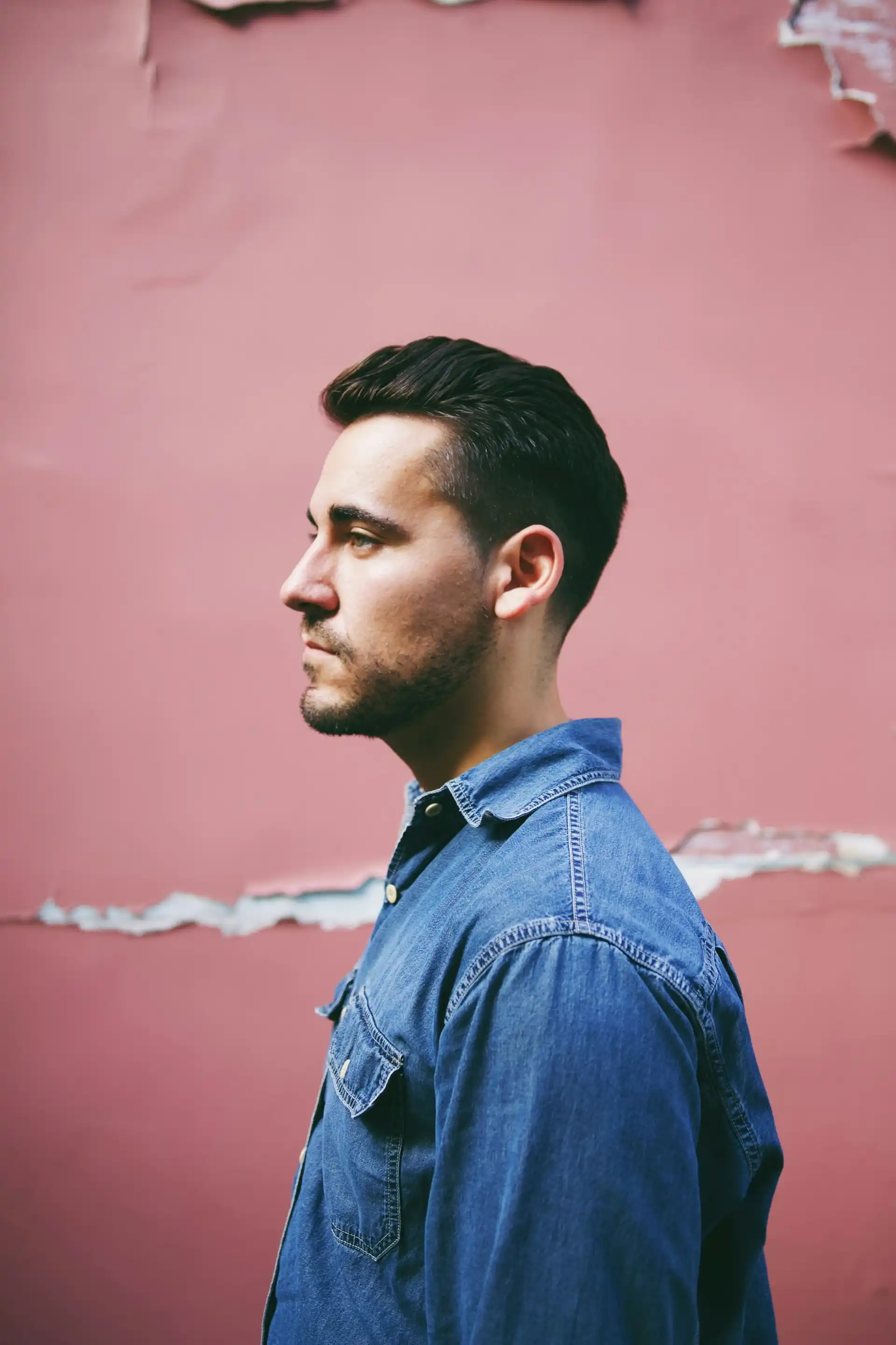 Un chico joven con cabello oscuro y una chaqueta vaquera está de pie de lado.