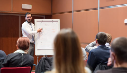 Young man in suit during presentation with clients is showing something on board