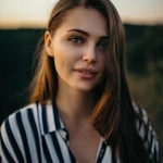 Woman with blonde hair smiling outdoors at sunset.