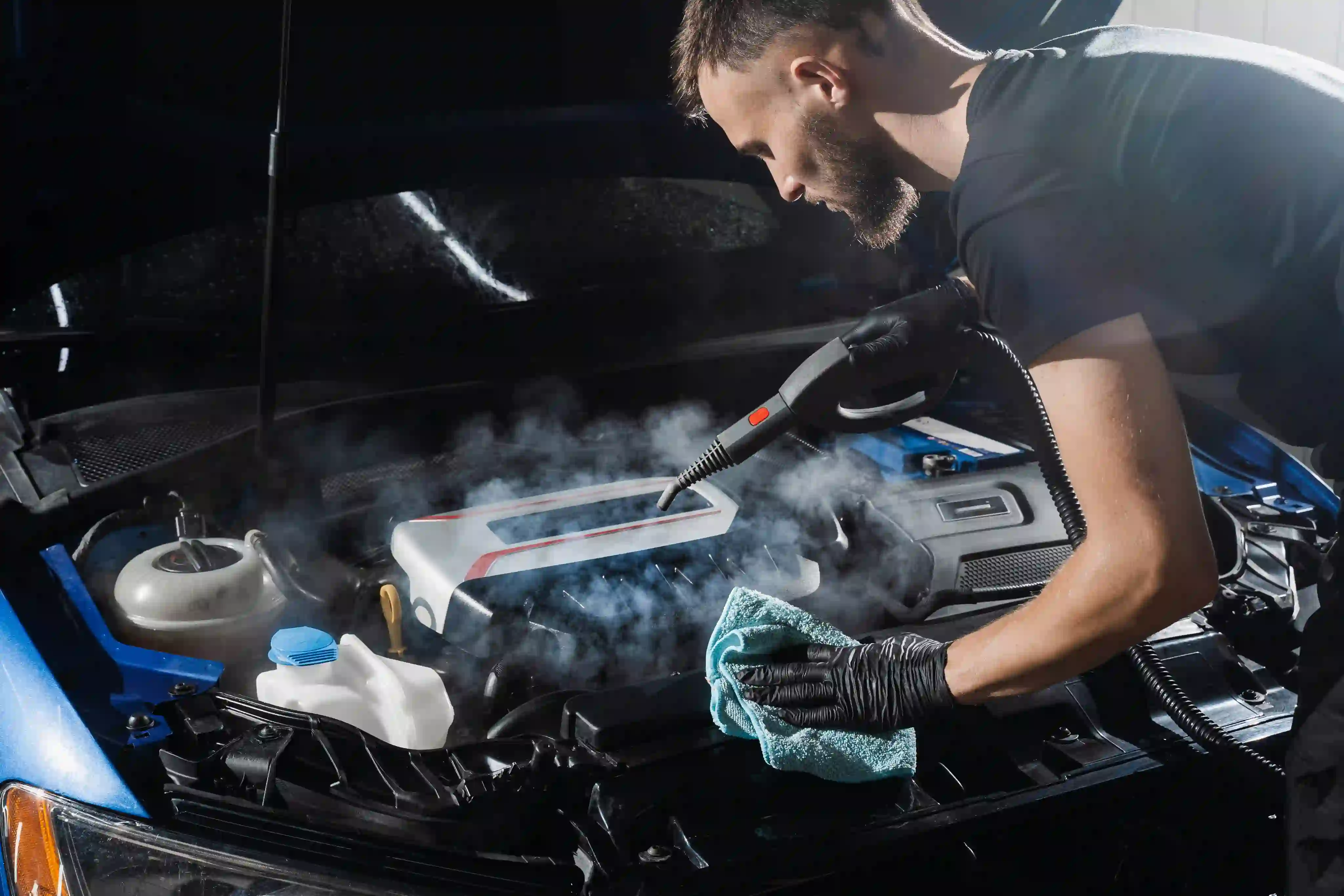 Person cleaning a car engine with steam and cloth