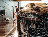 Car being washed with soap; person in background.