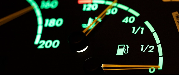 Close-up of a car dashboard showing a speedometer and fuel gauge, both illuminated in green. 