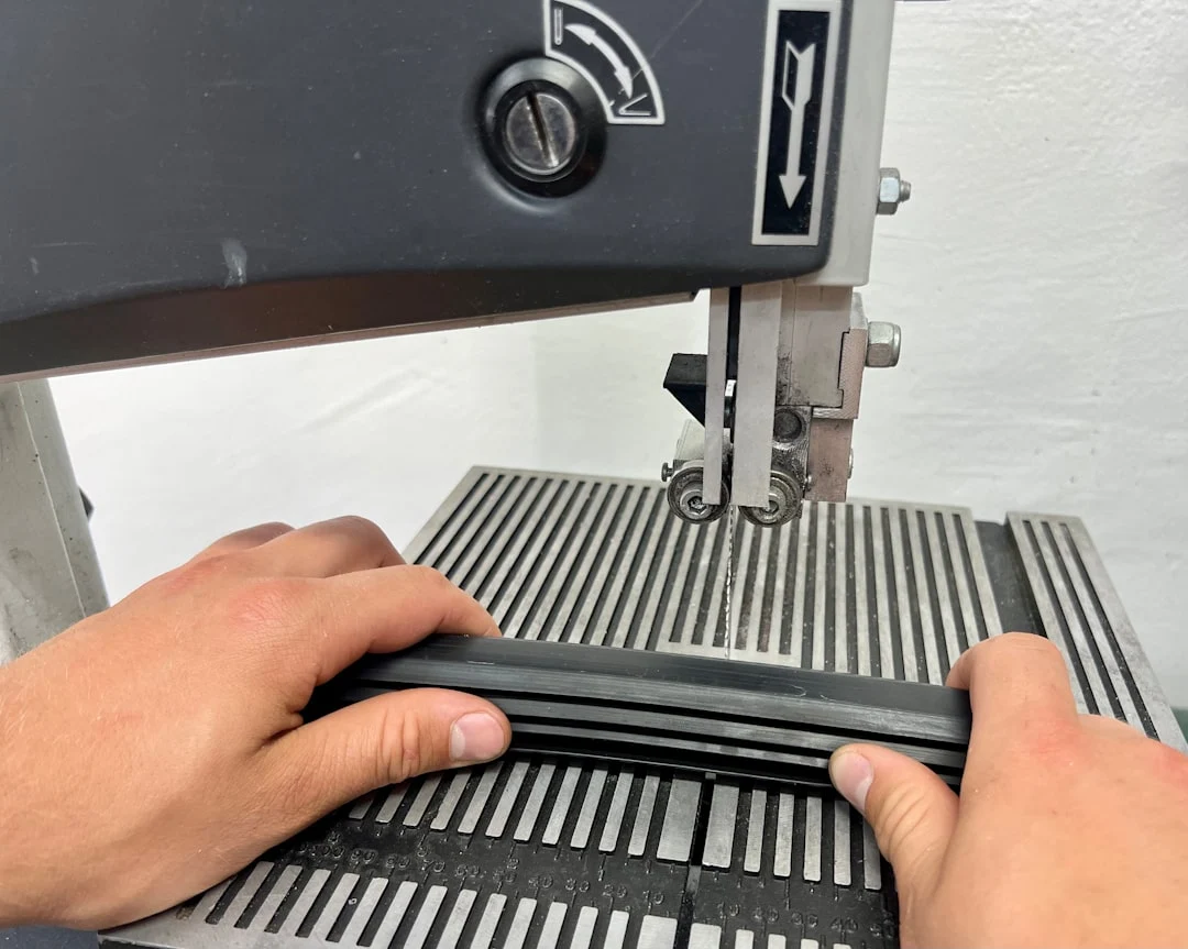 Hands operating a bandsaw with material being cut.