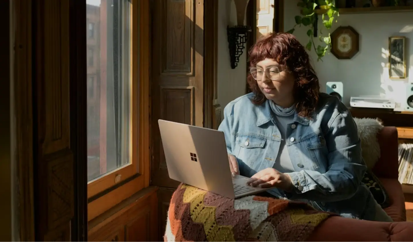 A girl in glasses and a denim jacket sits at a laptop